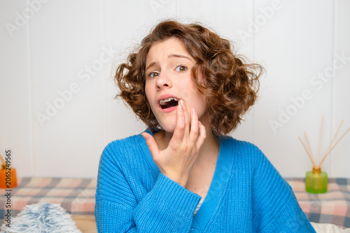 young woman with dental braces experiencing toothache or gum pain, touching her cheek with a concerned expression, needing dental care or relief