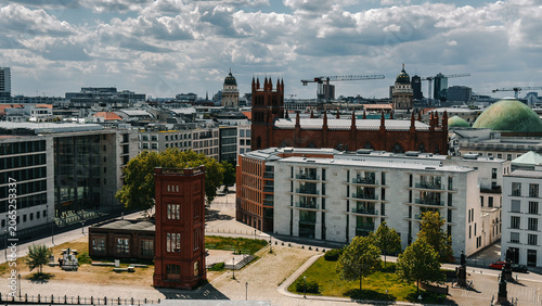 Berlin cityscape with historic red brick church, modern architecture, green trees and dramatic cloudy sky overlooking the urban skyline of Berlin Germany