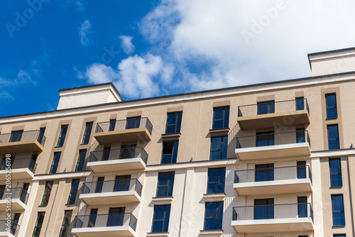 Modern apartment building facade with balconies against a blue sky. Urban