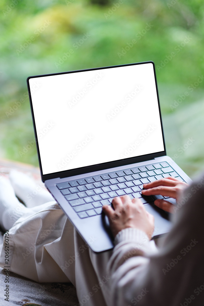 Fototapeta premium Vertical mockup image of a woman working on laptop computer with blank desktop white screen on the bed at home