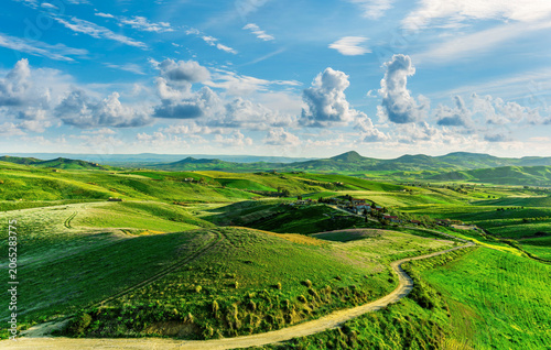 Cuadro en lienzo green flowering spring hills in countryside valley with rustic village road amon