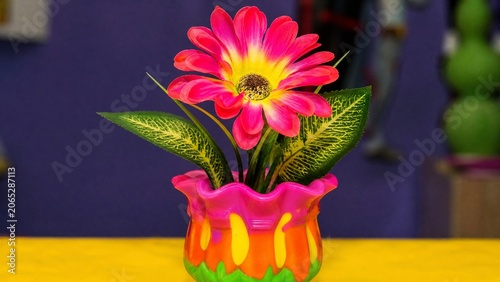 A cheap plastic flower in a garish vase, tacky aesthetic with bright colors.