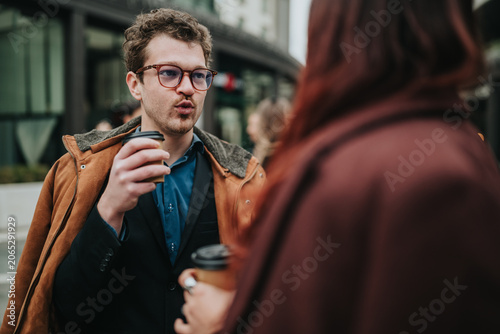 Obraz na plátně A young man and woman chat while holding takeaway coffee during a winter business meeting