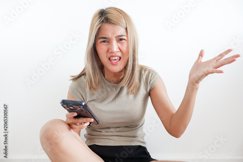 Frustrated young woman with smartphone reacts angrily to a problem or digital issue.