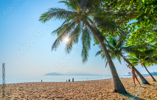 Sunny morning at Nha Trang Beach, Vietnam, where a visitor plays beach volleyball beneath swaying coconut palms beside the crystal-clear sea. A relaxing tropical scene showcasing an active beach lifes