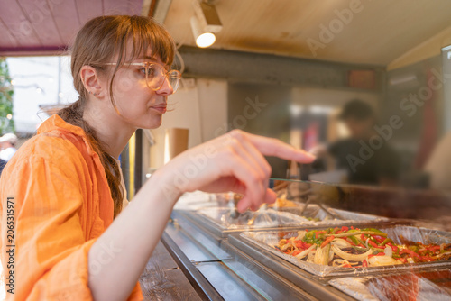 Woman orders food from a food stall in an outdoor market during a sunny day in a city