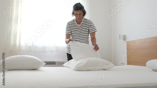 Senior woman putting fresh bed linen and pillowcases on a neatly prepared bed