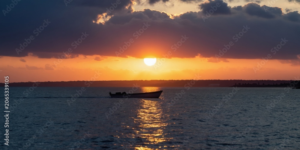 Fototapeta premium Small boat moves on calm sea water during golden sunset. Dark clouds gather above orange horizon line. Peaceful evening journey over ocean surface.