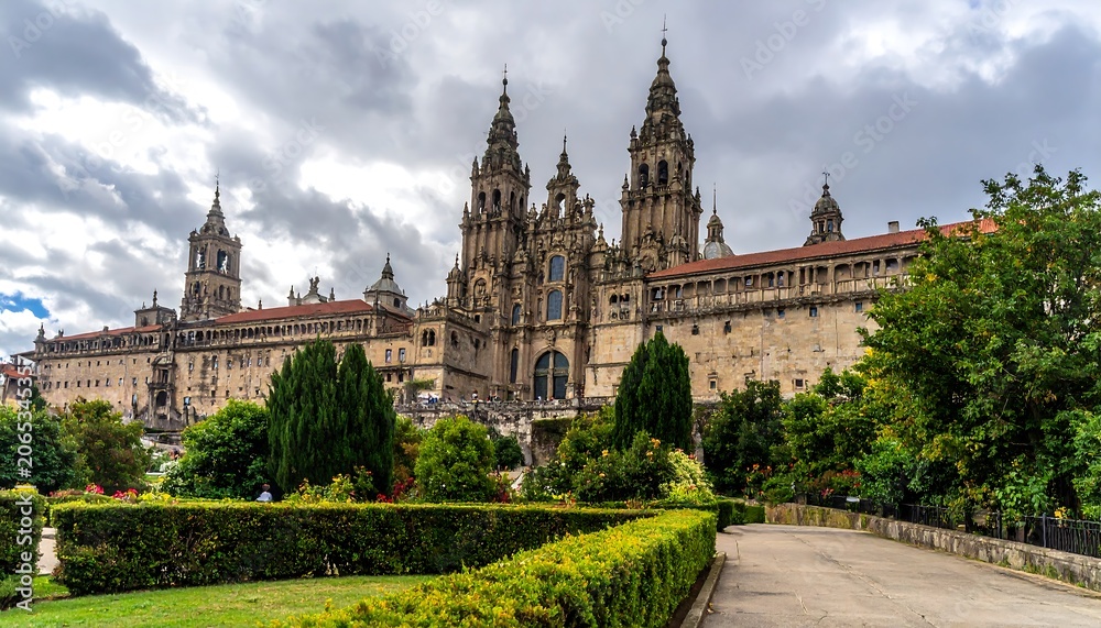 Fototapeta premium A large, ornate stone building with multiple spires and towers surrounded by lush greenery and a well-manicured garden under a cloudy sky