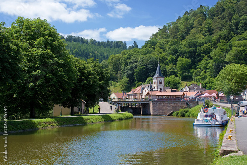 Lutzelbourg mit der St.-Michael-Kirche und dem Rhein-Marne-Kanal, auf dem ein Hausboot zu sehen ist