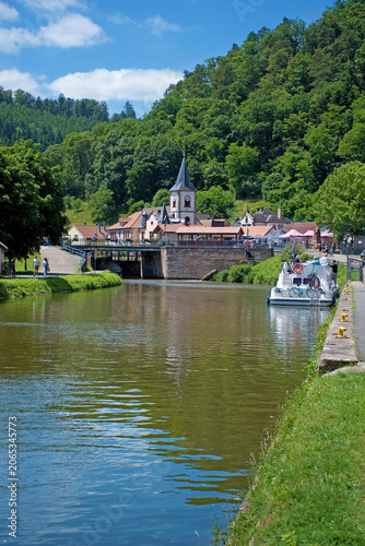 Lutzelbourg mit der St.-Michael-Kirche und dem Rhein-Marne-Kanal, auf dem ein Hausboot zu sehen ist