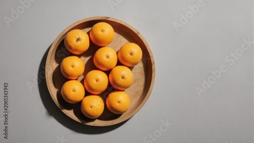 Overhead view of a wooden plate filled with vibrant, orange, fruit, against a gray backdrop