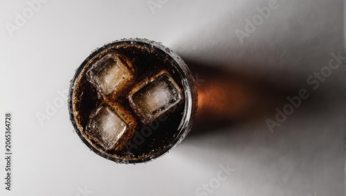 Overhead view of a chilled, dark beverage in a glass with ice cubes and shadow on a white surface