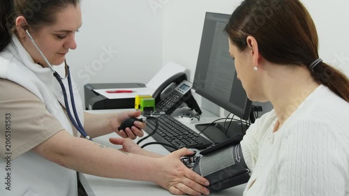 Positive doctor comforts patient during blood pressure monitoring in clinic. Medic conducts appointment with mature woman in hospital slow motion