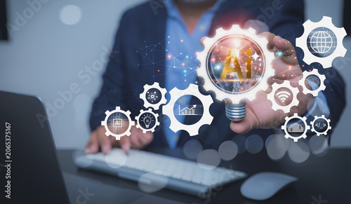 A businessman works on a laptop while holding a glowing lightbulb wrapped in a digital gear representing artificial intelligence.