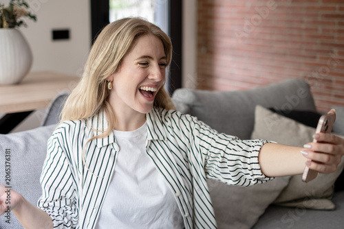 Canvastavla Young adult woman laughing loudly while relaxing on a sofa, holding a smartphone