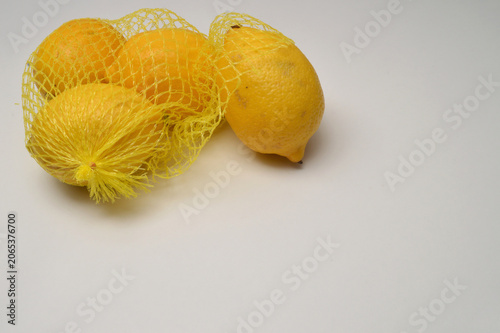 yellow lemon in a yellow mesh  on a white background corner composition horizontal layout, lemons close up with generous copy space,
