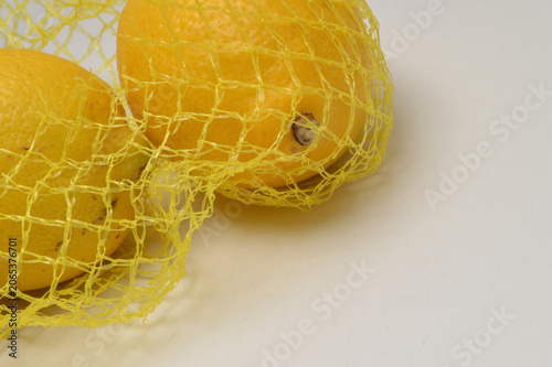 yellow lemon in a yellow mesh  on a white background corner composition hoirzontal layout, lemons close up with generous copy space,