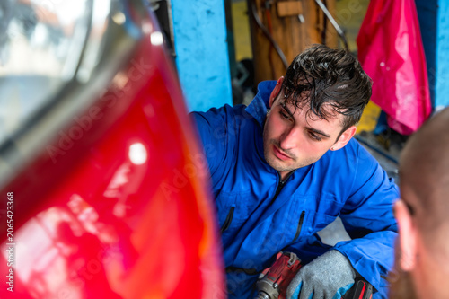 Cuadro en lienzo Handsome  male auto mechanic in uniform focusing on repairing and maintaining ca