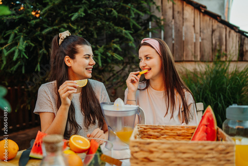 Young women enjoying fresh fruit and making orange juice outdoors