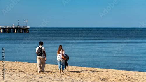 Couple walking on sandy beach toward calm Baltic Sea on sunny morning