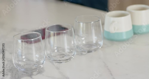 Camera adjusting focus stabilizing, 3 glasses shifting on marble top, phone under left, mugs right