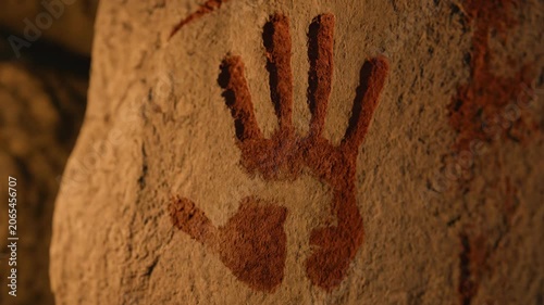 Primitive caveman human hand pressing red paint handprint onto cave wall in warm torchlight. Stone Age ancient art creation prehistoric culture concept.