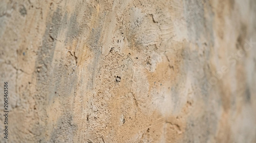 Close up macro shot of a rough textured beige and gray plaster wall showing details of peeling paint and aged surface background