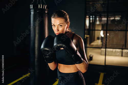 фотографія Female boxer wearing black gloves and sportswear poses confidently in a boxing g