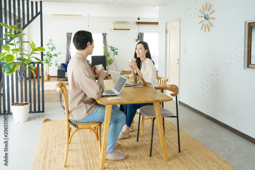 自宅のテーブルでノートパソコンで作業をする男性とマグカップを持つ女性の若い日本人パワーカップル