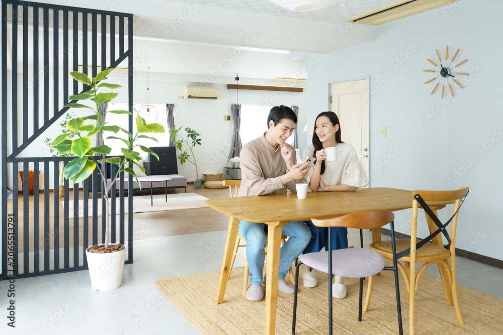 Fototapeta premium 自宅のテーブルでスマホを見ながら飲み物を飲む若い日本人パワーカップル