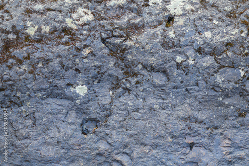 Dark, uneven stone reveals coarse texture and organic imperfections. Pale lichen patches contrast with deep fissures, conveying raw, enduring natural strength