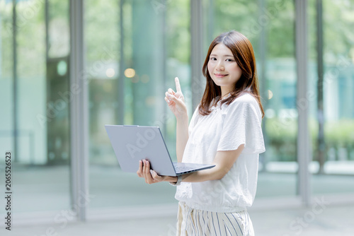ノートパソコンを持ちながら指差しをする日本人女性