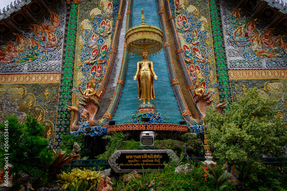 Fototapeta premium Stunning buddhist temple exterior with colorful mosaics and golden statue surrounded by lush greenery