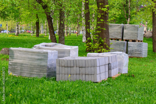 Neatly bundled stone blocks contrast with lush grass and birch trees. Scene conveys preparation for public space improvement and thoughtful landscaping