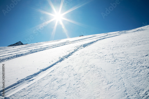Φωτογραφία Bright winter sun shining over snowy mountain slope with ski tracks mountain sun