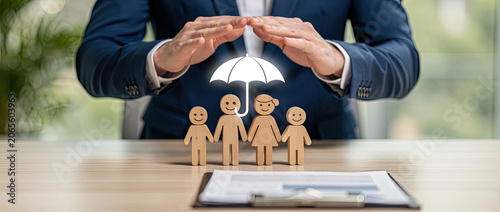 Family Insurance Protection: Businessman's Hands Shielding Wooden Family with Umbrella