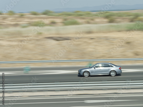 Car drives fast on highway in dry landscape during daylight with clear blue sky in the background