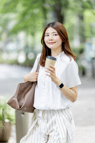 オフィス街でテイクアウトコーヒー持つ日本人女性