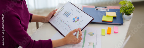 Young Asian professional analyzing colorful business charts and data reports at modern bright office workspace