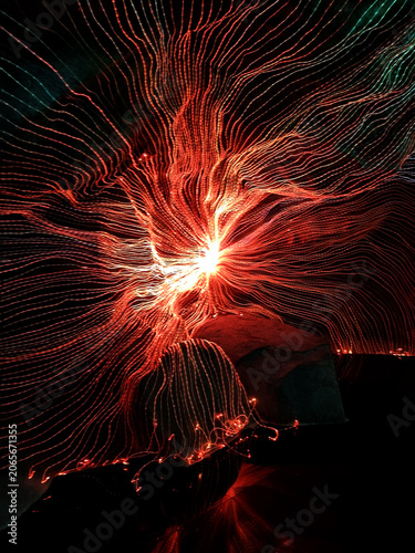 Abstract long exposure light painting with glowing red and orange fiber optic strands over rocks. Dynamic energy burst and data connection concept in dark environment. Modern artistic background.