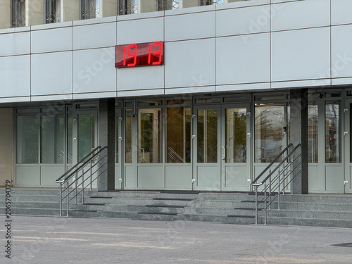 Billede på lærred Modern office entrance with access doors, stairways and digital clock display on building facade in urban business environment