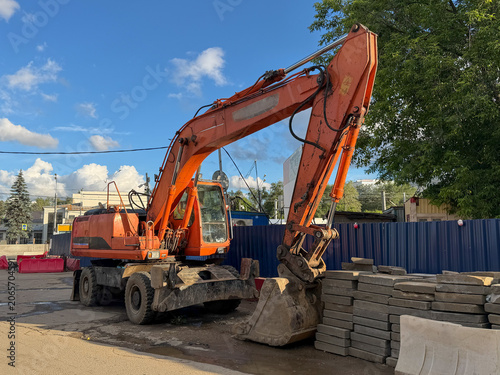 Photography Orange excavator stands at construction site in Moscow beside stacked paving stones