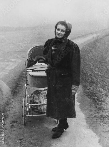 Authentic vintage motherhood archive photo of young woman with baby stroller outdoors