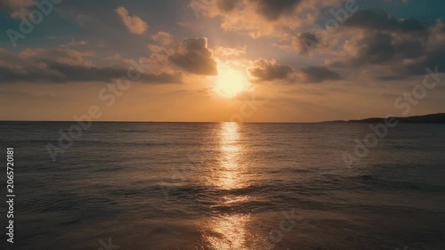 Golden sunset over calm ocean with distant coast, diffused light & scattered clouds