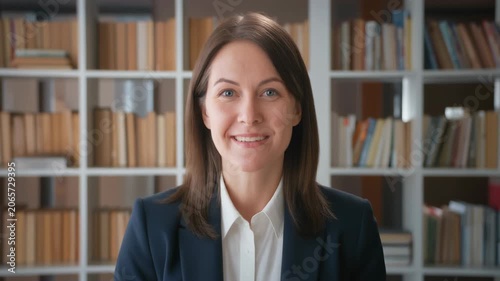 Smiling woman with blue eyes, blazer, and white shirt in front of bookshelf