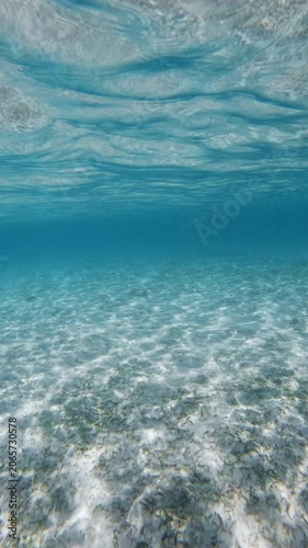 Crystal blue ocean underwater and sandy sea bottom with waves on surface