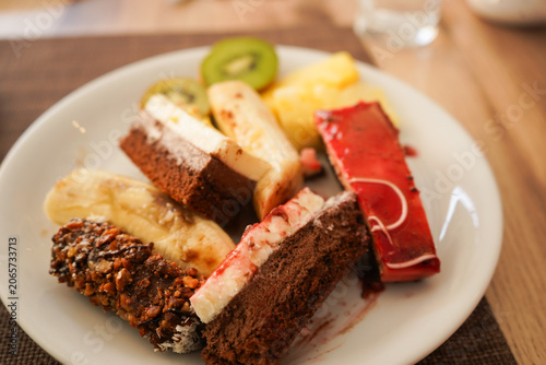 A loaded dessert plate from a hotel holiday buffet featuring assorted chocolate cakes, pastries, kiwi, and banana. Authentic all-inclusive resort dining and sweet indulgence concept.