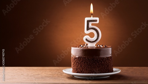 birthday chocolate cake with burning candle as a number five on brown background