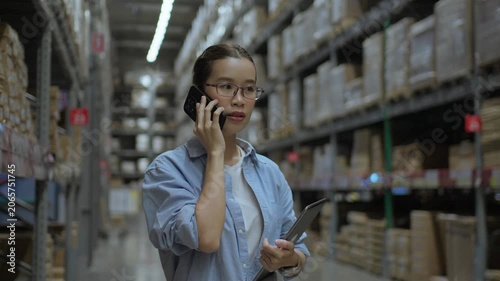 Female Warehouse Employee Communicating by Phone During Inventory Operations. Logistics communication, warehouse coordination, supply chain management